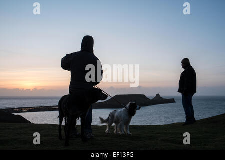 Dog Walker Silhouette mit zwei Hunden bei Sonnenuntergang an einem bitter kalten, sonnigen und windigen Tag des Wurms Kopf, Gower Halbinsel, Wales, UK. Stockfoto