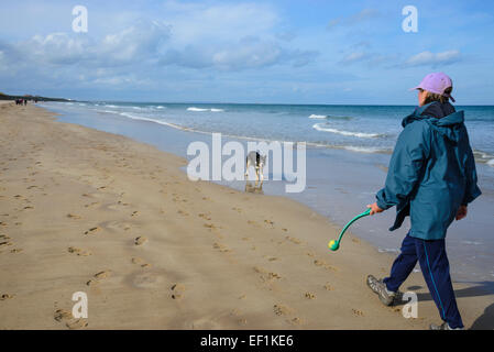 Frau und Border Collie Hund Ballspiele am Strand von Bamburgh, Northumberland, England Stockfoto