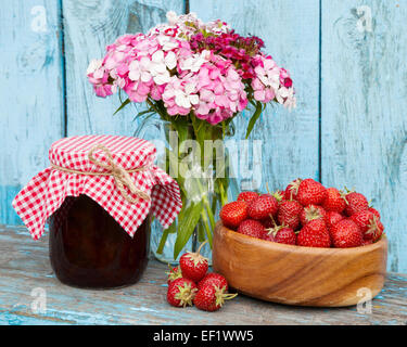 Erdbeeren in Holzschale, Blumenstrauß Garten und Marmelade auf Holzbrett Stockfoto