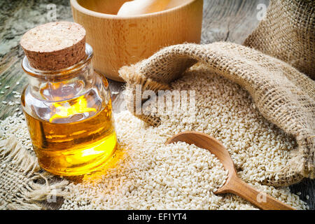 Sesam in Sack und Ölflasche auf rustikalen Holztisch Stockfoto
