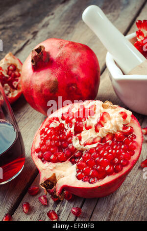 Granatapfel, Saft im Glas, Mörser und Stößel auf rustikalen Holztisch Stockfoto