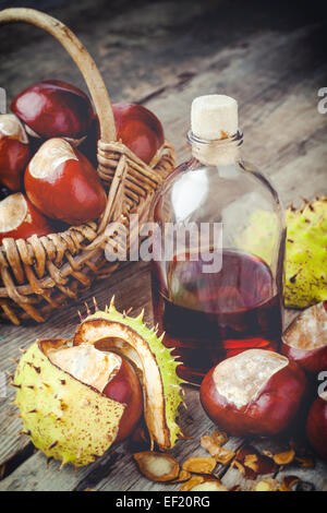 Maronen im Korb und Flasche mit Tinktur auf Holztisch Stockfoto