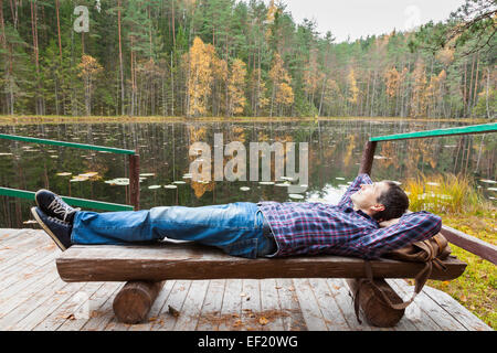 Junge männliche Wanderer ruht in der Nähe von See im herbstlichen Wald Stockfoto