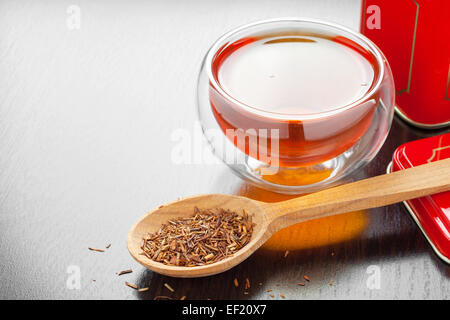 Rooibos in Löffel Closeup, zwei Teetassen und Tee Blechdose auf Küchentisch Stockfoto
