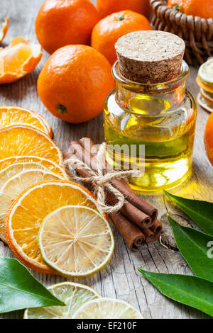 Eine Flasche wesentlich Zitrusöl, getrocknete Orange und Zitronenscheiben, Zimtstangen und Reife Mandarinen auf alten Tisch. Stockfoto