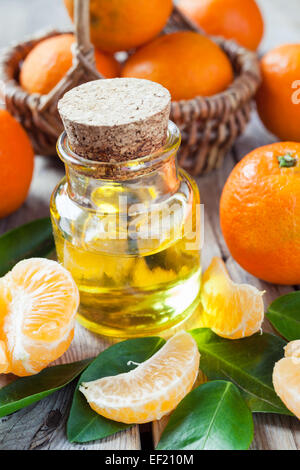 Flasche wesentlich Zitrusöl und Reife Mandarinen in Korb am alten Holz Küchentisch. Stockfoto