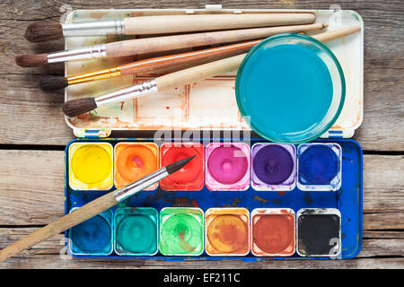 Satz von Aquarellfarben, Pinsel und Glas Wasser auf alten Holztisch. Ansicht von oben. Stockfoto