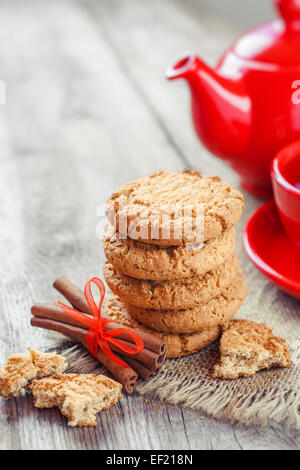 hausgemachte Kekse, Zimt Stöcke, rote Teekessel und Tasse Tee auf alten Tisch Stockfoto