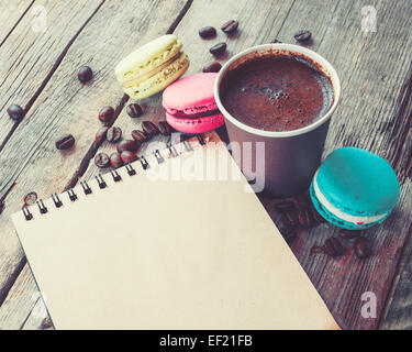 Makronen Plätzchen, Espresso Kaffee Tasse und Skizzenbuch auf rustikalen Holztisch, Vintage stilisierte Foto Stockfoto