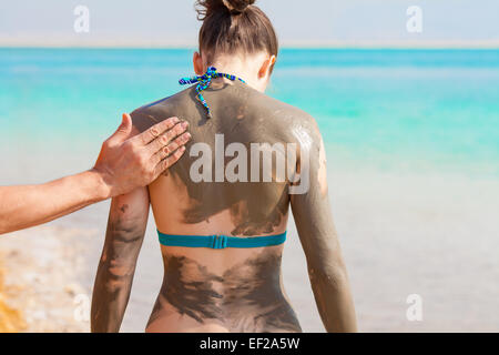 Junge hübsche Frau schmierte mit Schlamm am Strand Stockfoto