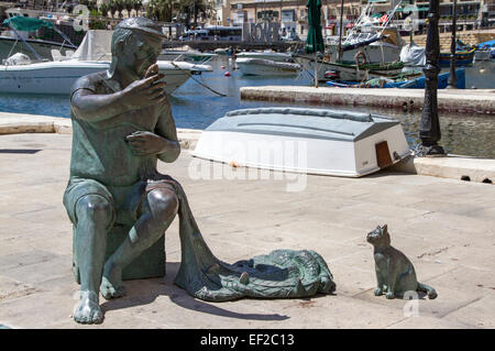 Eine Statue eines Fischers mit seinen Netzen und eine Katze warten auf Fisch auf der Hafenseite in St. Julian's Bay, Malta Stockfoto