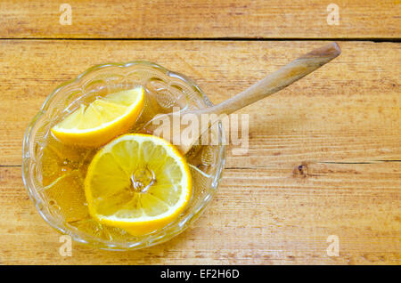 In Scheiben geschnittenen Zitrone in eine Glasplatte gefüllt mit Honig auf einem Holztisch gelegt Stockfoto