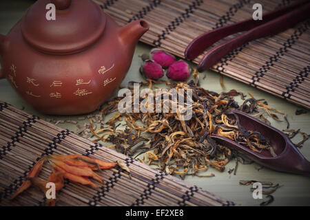 Dian Hong Mao Feng Tee. Grüner Tee Blätter mit Ton-Teekanne und Holzlöffel auf einem Tee-Tisch. Stockfoto