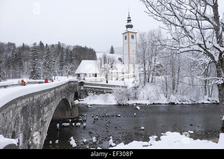 Ribčev Laz, Kirche St. Johannes der Täufer und Stein Brücke über den Fluss Sava Bohinjca im winter Stockfoto