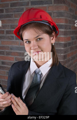 junge weibliche Bau Ingenieur tragen rote Helm und Anzug an der Vorderseite Ziegelmauer Stockfoto