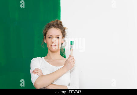 junge Frau stand vor einer selbst bemalten Wand mit einem Pinsel Stockfoto