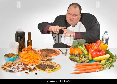 Übergewichtiger Mann sitzt an einem Tisch voller Essen Stockfoto