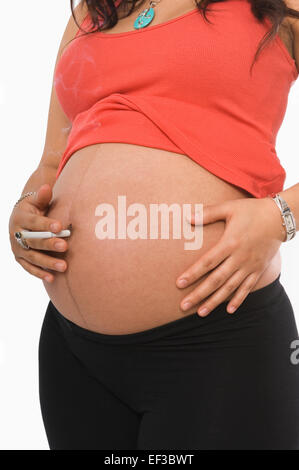 Schwangere Frau hält eine Zigarette vor ihrem Bauch Stockfoto