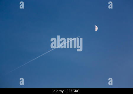 Spur der Düsenjet in den blauen Himmel mit dem Mond auf einem Hintergrund Stockfoto