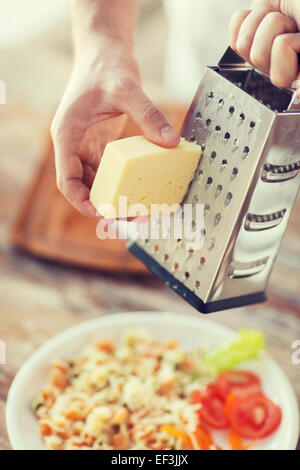 Nahaufnahme von männlichen Händen reiben von Käse über Nudeln Stockfoto