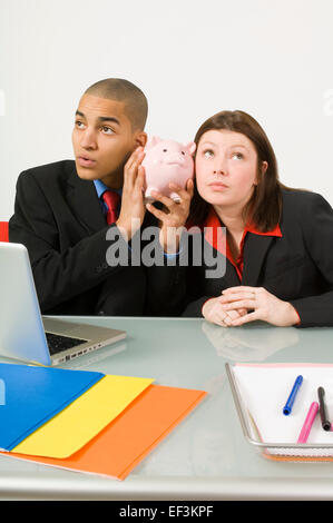 Kollegen halten Sparschwein für ihre Ohren Stockfoto