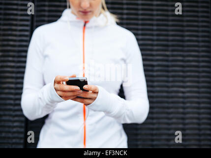 Bild der Frau in der Sportswear mit Handy zugeschnitten. Konzentrieren Sie sich auf Hände und Smartphone. Stockfoto