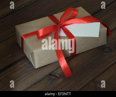 Vintage Geschenkbox verpackt in Kraftpapier und rotes Band auf hölzernen Hintergrund Stockfoto