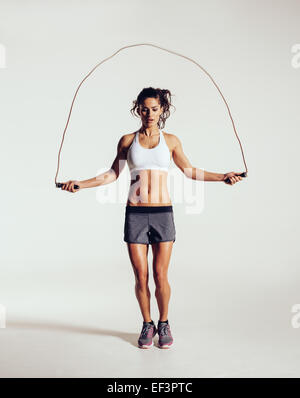 Passen Sie junge Frau Springseil. Porträt der muskulöse junge Frau Training mit Seilspringen auf grauem Hintergrund. Stockfoto