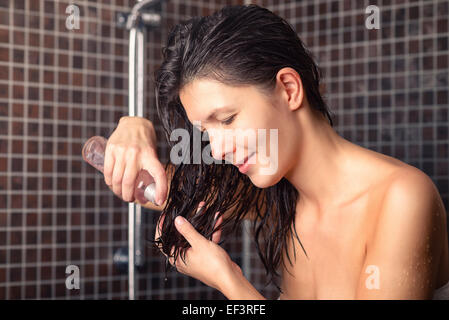 Junge Frau zu ihr neu Haaröl zuweisen gewaschen Haar stehen im Badezimmer in ein Handtuch Abgabe in ihrer hand Stockfoto