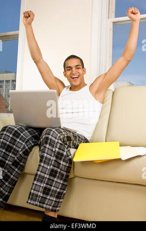 Glücklicher Mann sitzt auf der Couch mit laptop Stockfoto