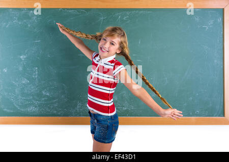 Geflochtene blonde Studentin spielen im grünen Tafel mit Zöpfen im Klassenzimmer Stockfoto