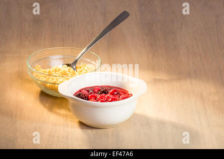 Beeren-Mix in Keramikschale mit Streusel in eine Glasschüssel mit einem Löffel auf den Tisch. Stockfoto