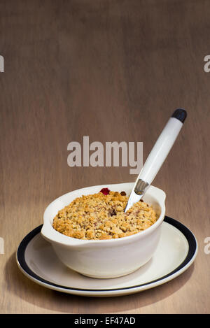 Eine Keramikschale mit frisch gebackenem gemischte Beeren Crumble und einem Löffel stecken der Beeren-Crumble. Stockfoto