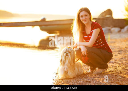 Junge Frau mit Shih-Tzu Hundesitting am Seeufer. Roten Abendlicht. Stockfoto