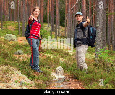 Junge Touristen-paar mit Hund Daumen auf Wald Hintergrund auftauchen. Stockfoto