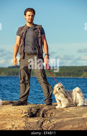 Junger Mann Tourist mit Shih-Tzu Hundewiesen am Seeufer. Stockfoto