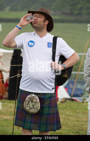 Ein Mann in einem schottischen Kilt trägt eine England Fußball-Shirt und ein Bierchen getrunken, während Ereignisse bei Bannockburn Live, Schottland. Stockfoto