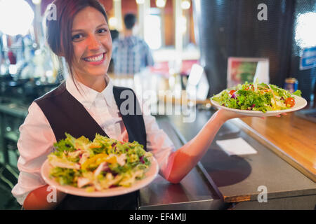 Hübsche Kellnerin hält Teller mit Salaten Stockfoto