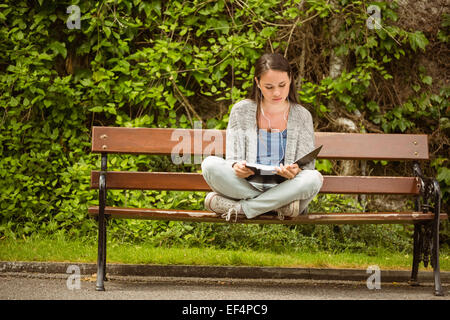 Schüler sitzen auf Bank Musik hören mit Handy und Überarbeitung Stockfoto