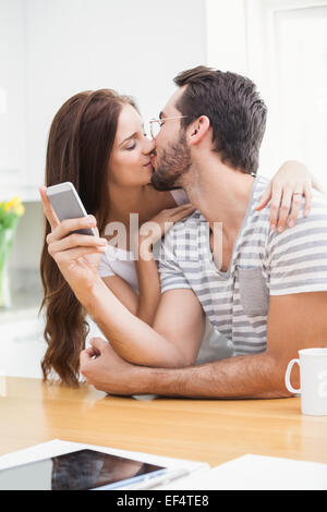 Junger Mann mit Smartphone, während Freundin ihn küsst Stockfoto