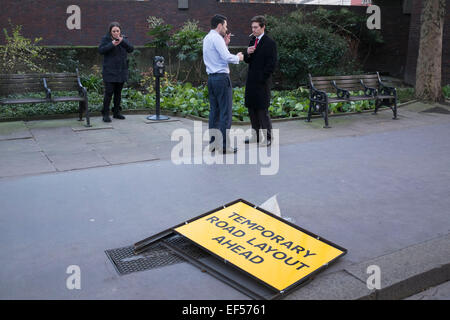 Drei Menschen rauchen auf der Straße vor einem Zeichen, das temporäre Road Layout Ahead liest. Zwei Männer ein Aufleuchten während der Frau während SMS raucht. London, UK. Stockfoto