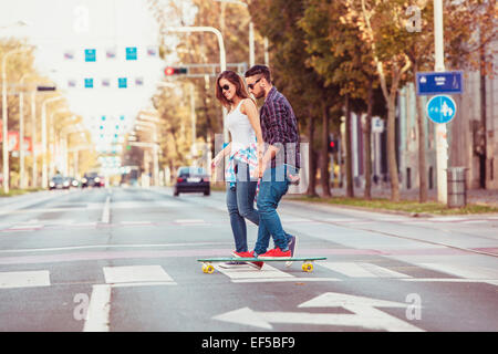 Junges Paar Skateboard über Zebrastreifen Stockfoto