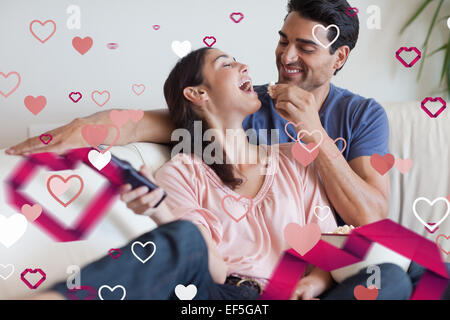 Zusammengesetztes Bild von verspielten paar vor dem Fernseher während des Essens popcorn Stockfoto