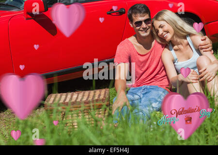 Zusammengesetztes Bild eines lächelnden Paares sitzen auf dem Rasen mit Picknick zusammen Stockfoto