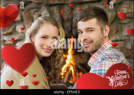 Zusammengesetztes Bild des Lächelns junges Paar vor brennenden Kamin Stockfoto