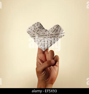 die Hand eines jungen Mannes hält ein Herz mit Papierstreifen mit dem Text happy Valentines Day mit einem Retro-Effekt Stockfoto