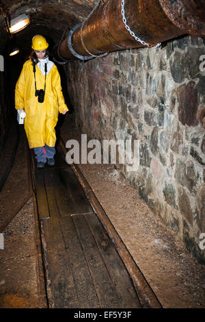 Weiblichen Erwachsenen Spaziergänge entlang der engen hölzernen Bahnen einen gelben harten Hut und Mantel in die Grube Bergwerk von 1156 bis 1993 im Einsatz Stockfoto