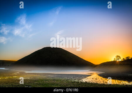 Der Nebel tritt beim Sonnenaufgang über dem historischen Denkmal der Silbury Hill in der Nähe von Avebury in Wiltshire. Stockfoto