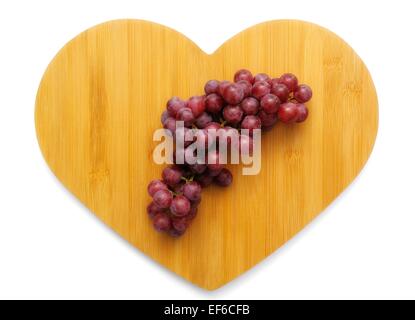 Rote Trauben auf einem Hintergrund aus Holz in Herzform Stockfoto