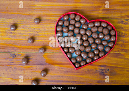 Herz geformten Box gefüllt mit kleinen Pralinen Kugeln mit vielen von ihnen verstreut auf dem Holztisch Stockfoto